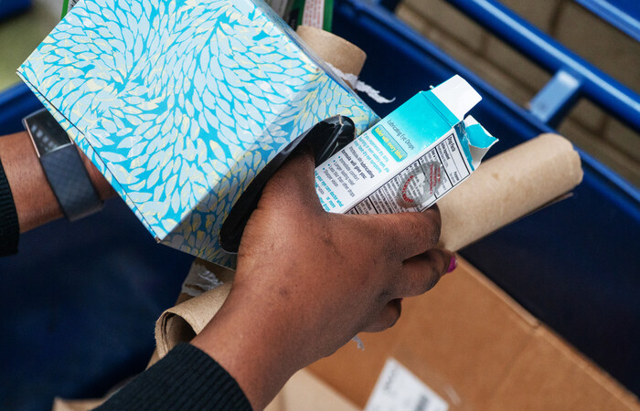 A person putting paper and cardboard items into a recycling bin.