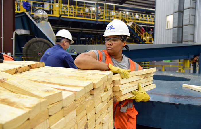 A woman holding lumber in a mill