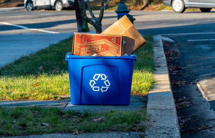 A pizza box in a blue curbside recycling bin.