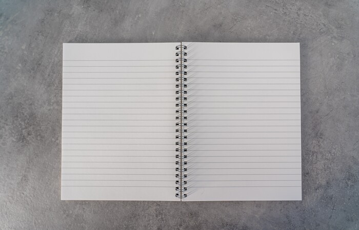 An open notebook with lined paper laying on a countertop. The notebook is blank. 