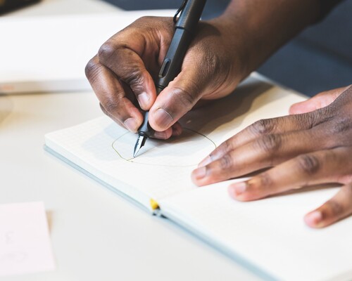 Individual uses a pen to sketch in a notebook.