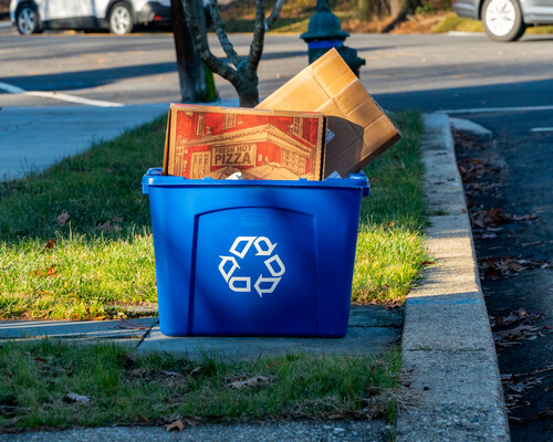 A pizza box in a blue curbside recycling bin.