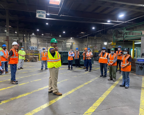 Levell Hairston wearing safety gear standing in the middle of a large circle of employees also wearing safety gear.