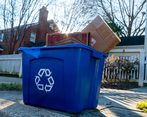 Paper products in blue recycling bin at residential curb.