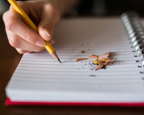 A person writing in pencil on notebook paper