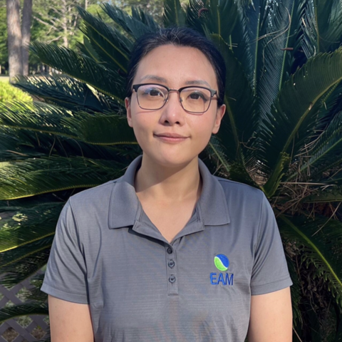 Hong Wilcoxon is wearing glasses and a polo. She's standing outside in front of plants.
