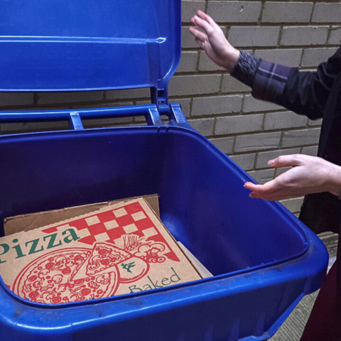 A pizza box in a recycling bin with a woman closing the lid