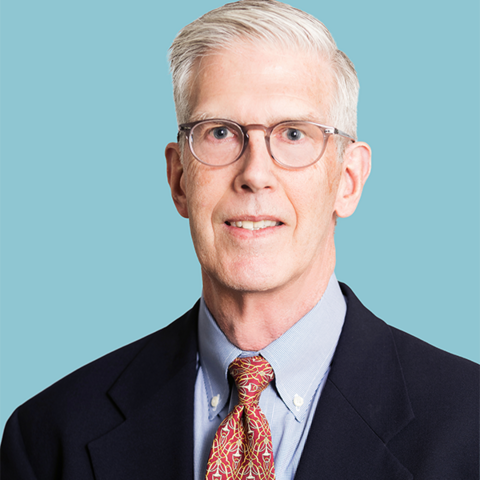 Mark Pitts has short, cropped grey hair and wears glasses. He's wearing a dark suit, light blue shirt and red tie.