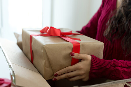 A woman removing a generically wrapped present from a cardboard box.